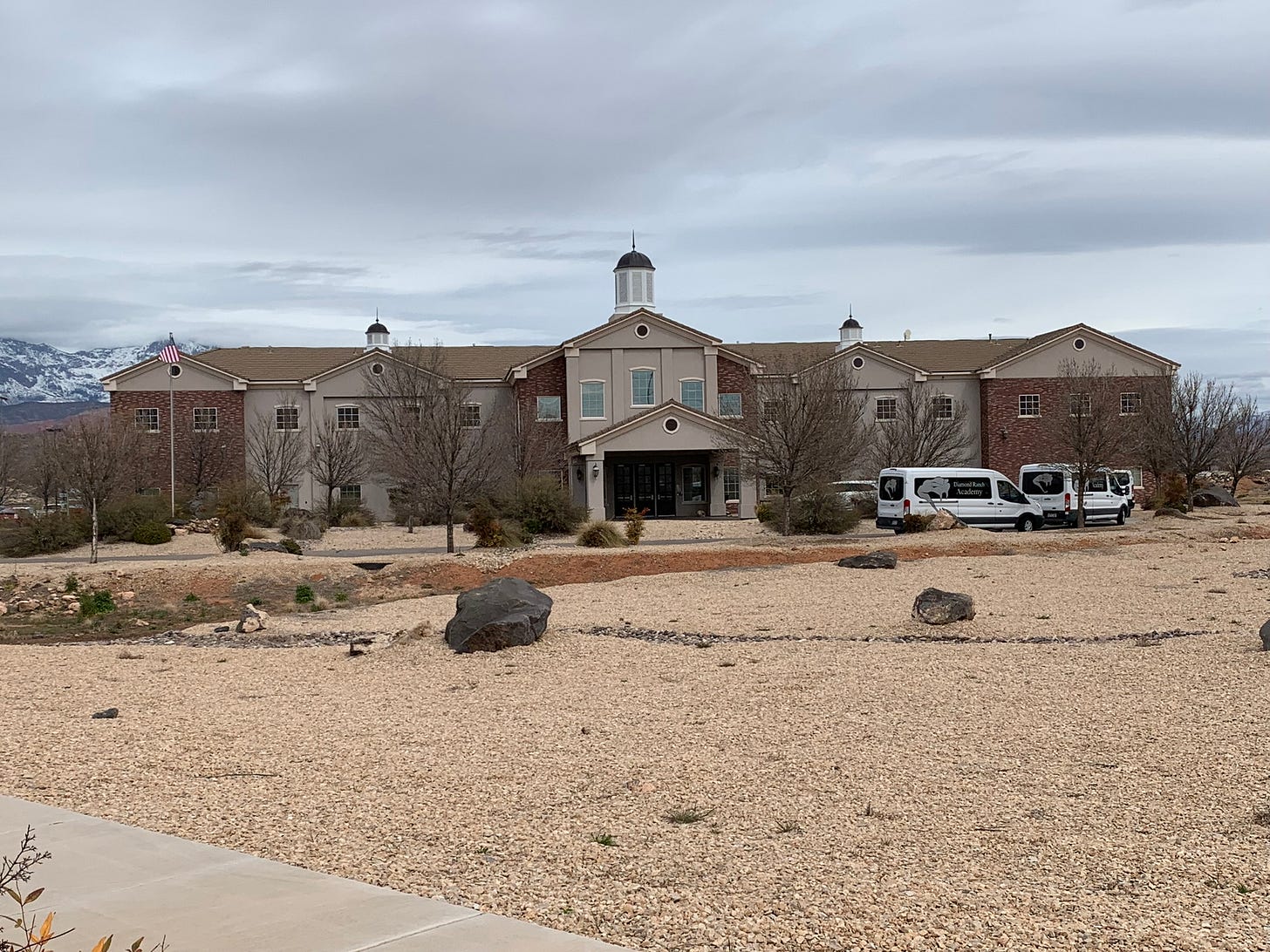 A tan and brick building, with vans parked in front of it