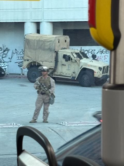 Picture taken through the public bus window of a national guard with a rifle standing in front of a graffiti'd white building with humvees next to it Picture taken through the public bus window of a national guard with a rifle standing in front of a graffiti'd white building with humvees next to it