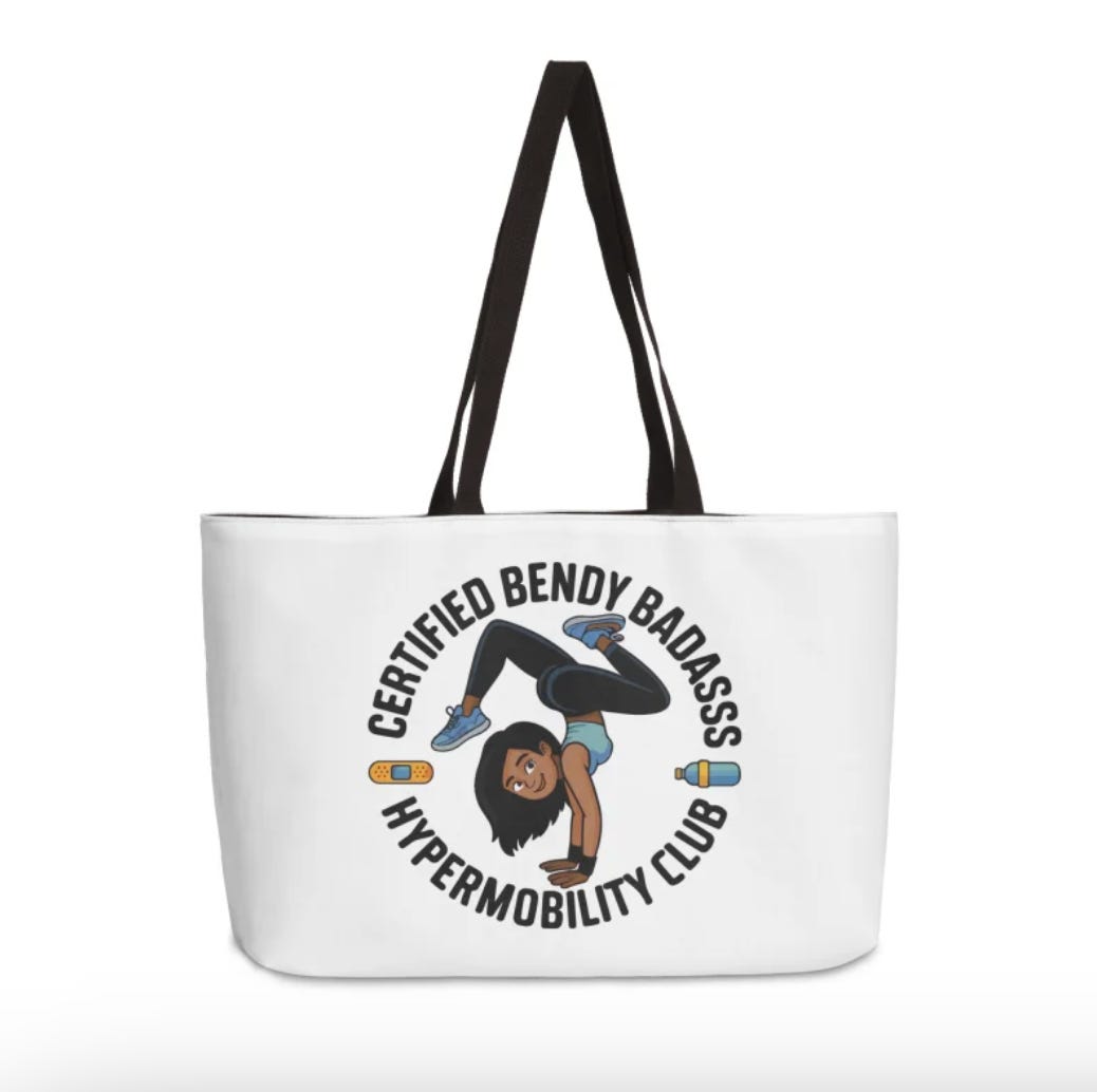 White tote bag with black straps featuring an illustration of a woman doing a cartwheel and text that reads “Certified Bendy Badass Hypermobility Club.”