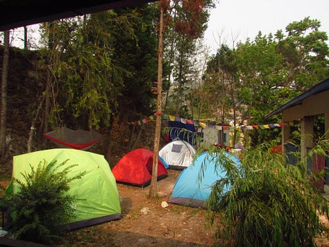 Pictures of life volunteering in disaster relief in Nepal. Tents in a courtyard, people sitting around reading books and playing games, standing on top of a damaged building, and buckets they used for washing.