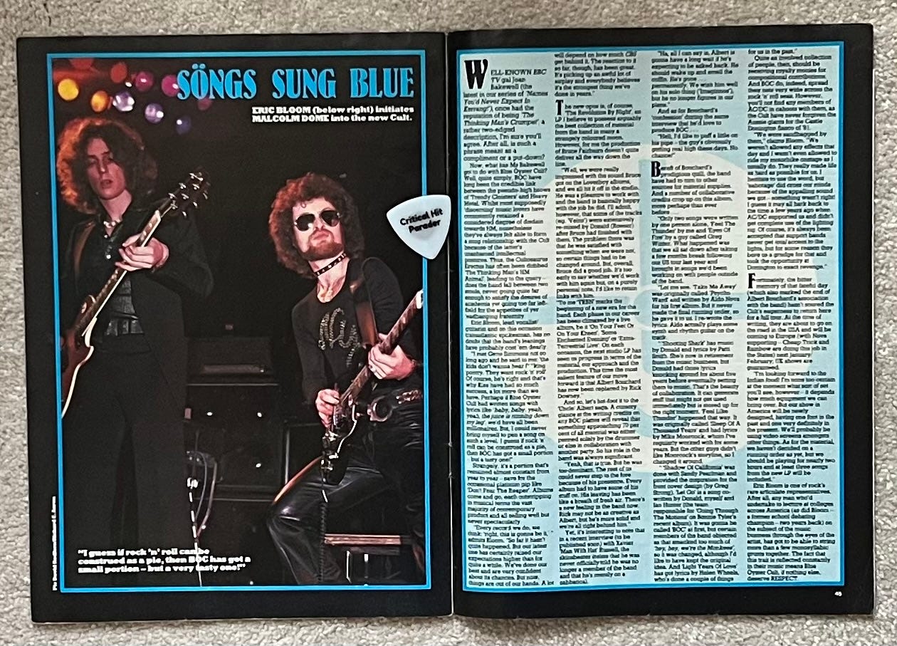 A two page spread from Kerrang magazine. The right side has a photo of Blue Oyster Cult in concert featuring menacingly frail Alan Lanier playing electric guitar and menacing Eric Bloom playing stun guitar. The right side has a bunch of text in small font on a blue background with a disproportionate cult sign. A white Critical Hit Parader lays on the magazine near the spine, enthralled by Bloom's shades.