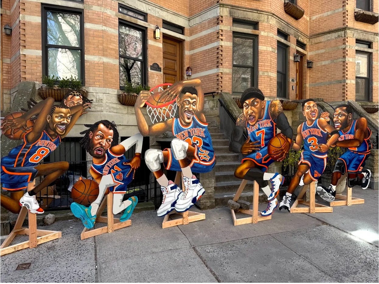 A stylized series of six life-size cut-out paintings of New York Knicks stars, displayed on the street in front of brownstone buildings in New York City