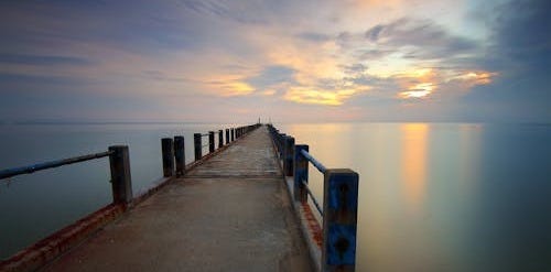 Free A tranquil view of a rusty jetty extending into calm waters during sunset, reflecting vivid sky colors. Stock Photo Free A tranquil view of a rusty jetty extending into calm waters during sunset, reflecting vivid sky colors. Stock Photo