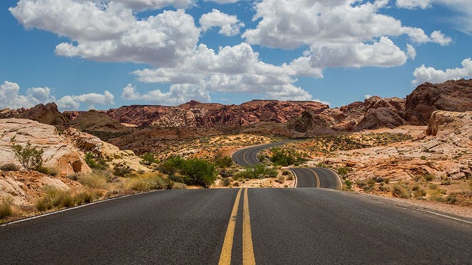 a highway curving toward the mountains under a beautiful blue sky