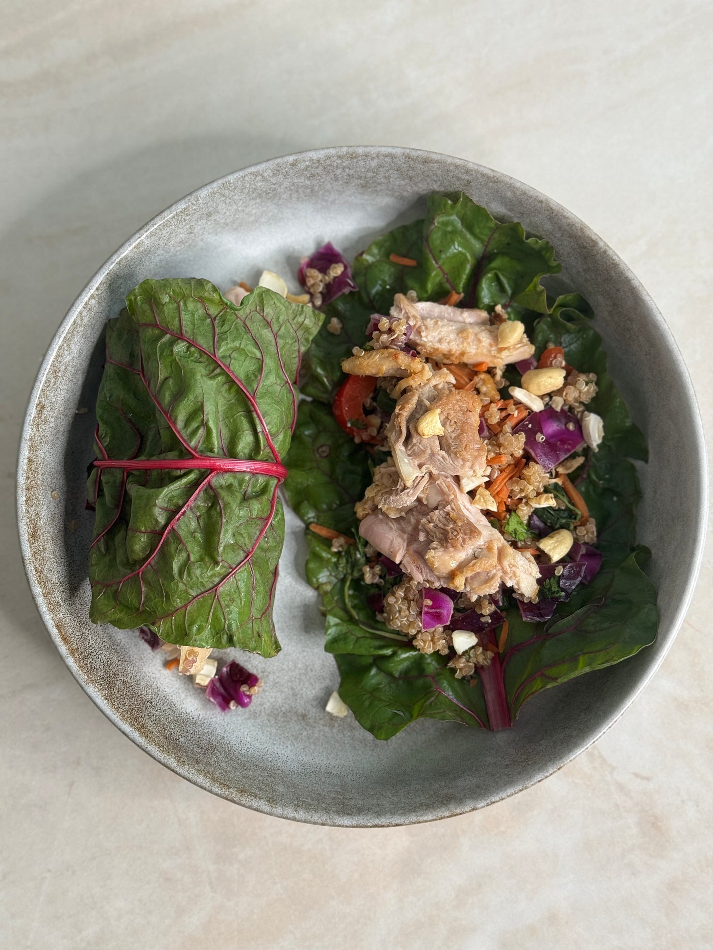 Colorful wraps made with Swiss chard, filled with quinoa salad, sautéed carrots, and sliced chicken, topped with crunchy cashews and a sesame-ginger dressing.