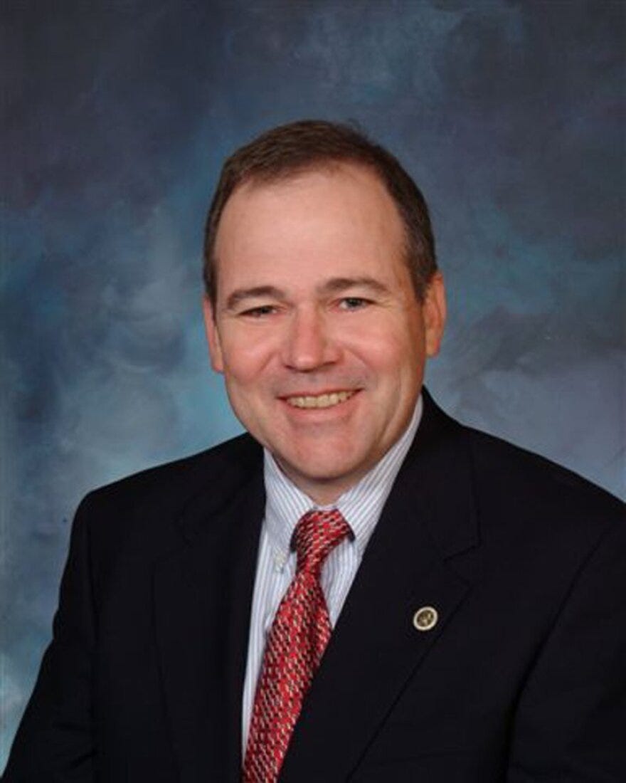 A man in a dark suit and a red tie, smiling