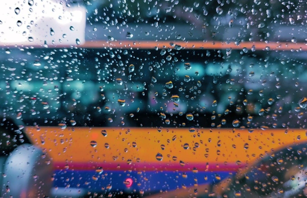 Raindrops on a bus window with warm, blurred bus in the background Raindrops on a bus window with warm, blurred bus in the background