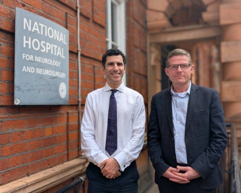 Rhys Hibbert stands with Hani Marcus outside the hospital, which is a red-brick building. Hibbert is 48, with short fair hair; he wears a pale blue shirt and dark blue suit jacket plus glasses. Rhys Hibbert stands with Hani Marcus outside the hospital, which is a red-brick building. Hibbert is 48, with short fair hair; he wears a pale blue shirt and dark blue suit jacket plus glasses.