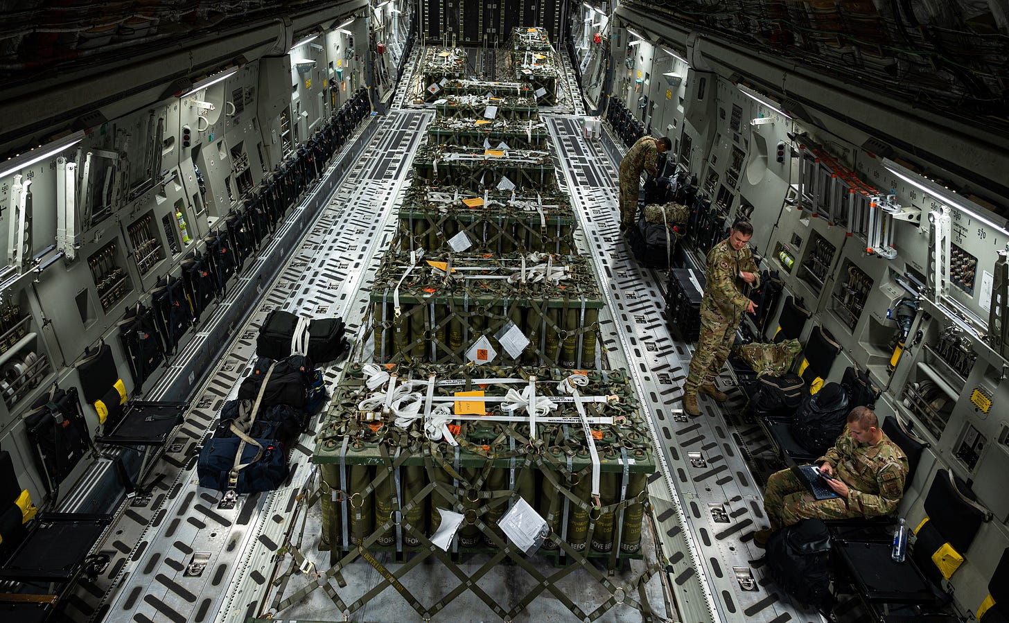 deck of a plane; containers wrapped in middle of floor stretching back; a few airmen sound over to the side deck of a plane; containers wrapped in middle of floor stretching back; a few airmen sound over to the side