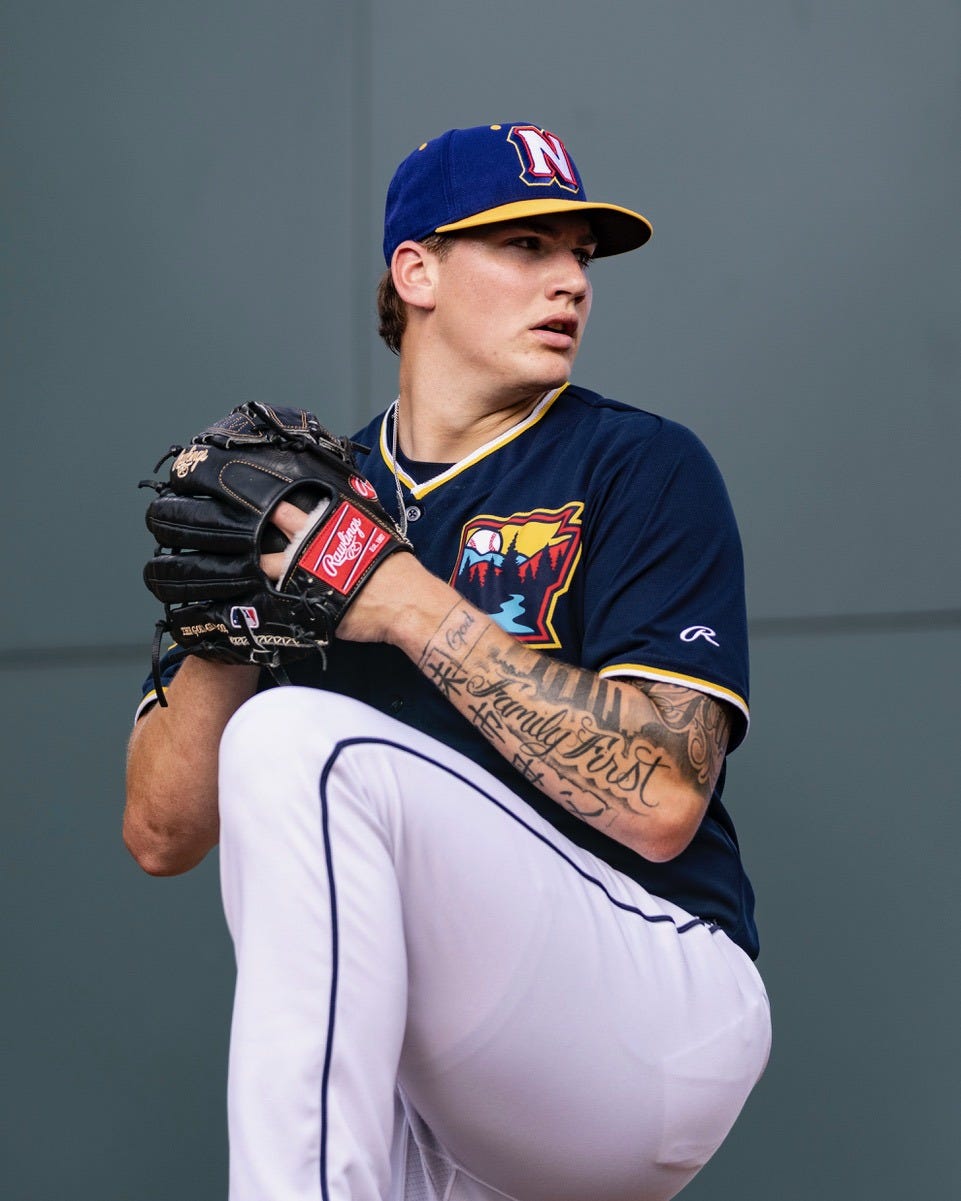 Right-handed pitcher Ben Kudrna winds up to throw a pitch while wearing white pants and a dark-colored uniform with a blue and yellow cap.