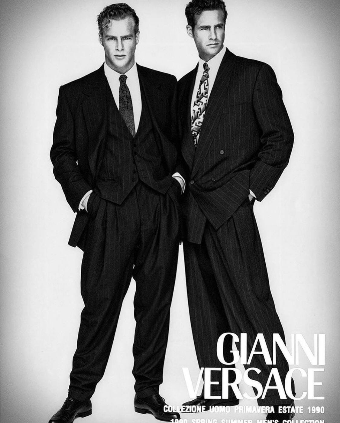 Two men in oversized suits post next to one another in a black and white photograph.