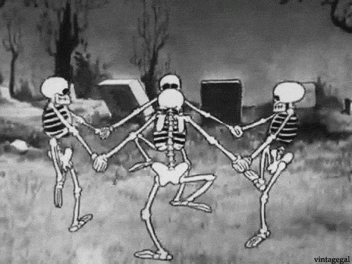 Un fotogramma in bianco e nero di un cartone animato d'epoca che mostra quattro scheletri stilizzati che danzano in cerchio in un cimitero. Gli scheletri si tengono per mano e sollevano le gambe in modo coordinato tra lapidi e alberi spogli sotto un cielo grigio. Lo stile d'animazione è quello classico degli anni '20/'30. Scena tratta dal celebre cortometraggio Disney "The Skeleton Dance" (La danza degli scheletri) del 1929. Quattro scheletri ballano tenendosi per mano in un cimitero buio, un esempio iconico dell'animazione "Rubber Hose" in bianco e nero. Un fotogramma in bianco e nero di un cartone animato d'epoca che mostra quattro scheletri stilizzati che danzano in cerchio in un cimitero. Gli scheletri si tengono per mano e sollevano le gambe in modo coordinato tra lapidi e alberi spogli sotto un cielo grigio. Lo stile d'animazione è quello classico degli anni '20/'30. Scena tratta dal celebre cortometraggio Disney "The Skeleton Dance" (La danza degli scheletri) del 1929. Quattro scheletri ballano tenendosi per mano in un cimitero buio, un esempio iconico dell'animazione "Rubber Hose" in bianco e nero.