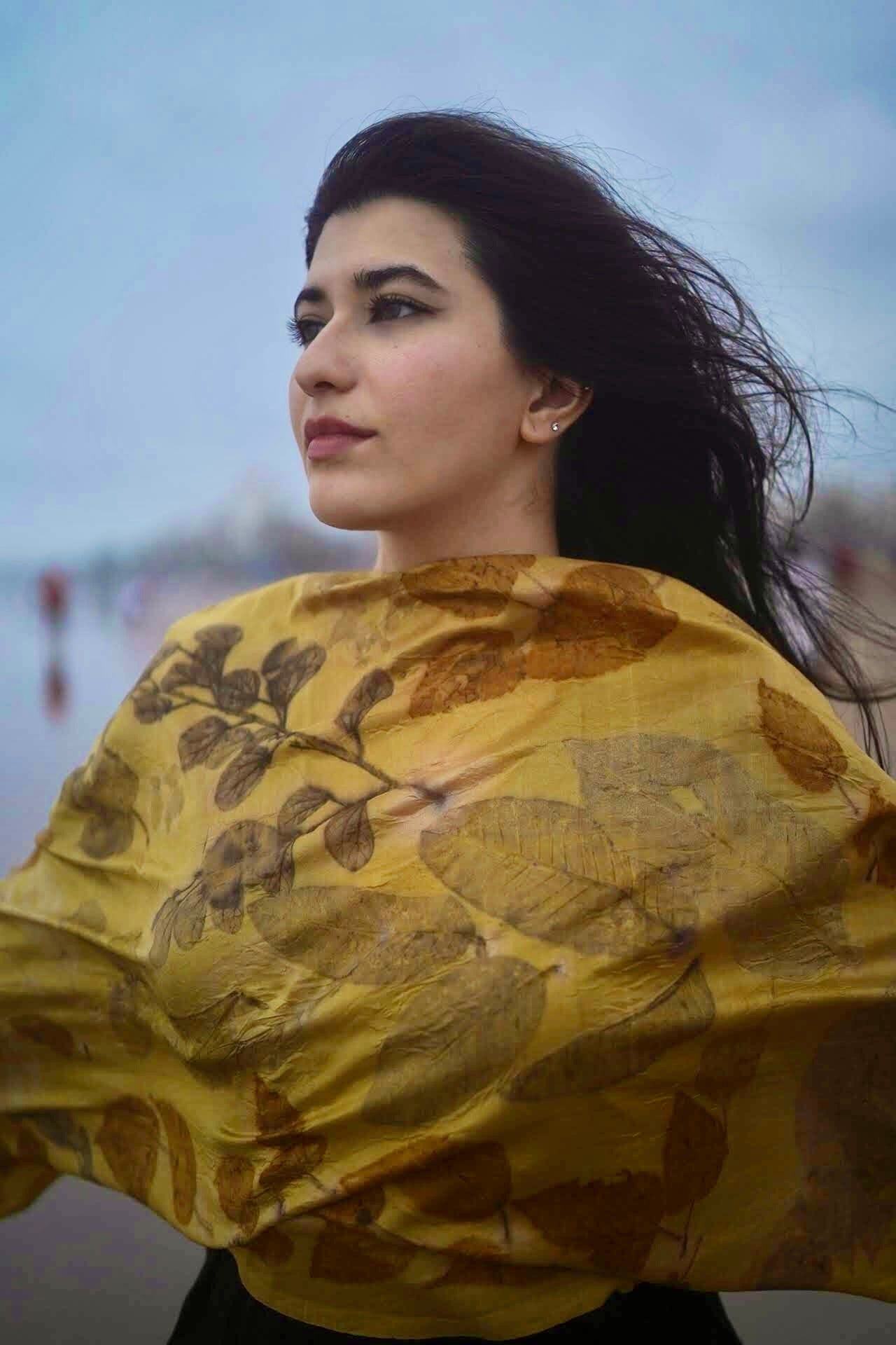 Woman wearing a yellow eco-printed scarf with leaf patterns, looking into the distance