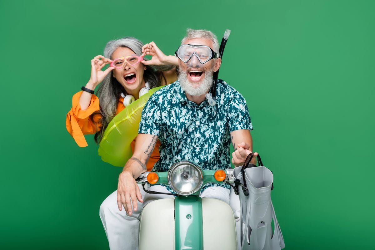 Multiethnic and excited middle aged couple in goggles riding moped isolated on green Multiethnic and excited middle aged couple in goggles riding moped isolated on green