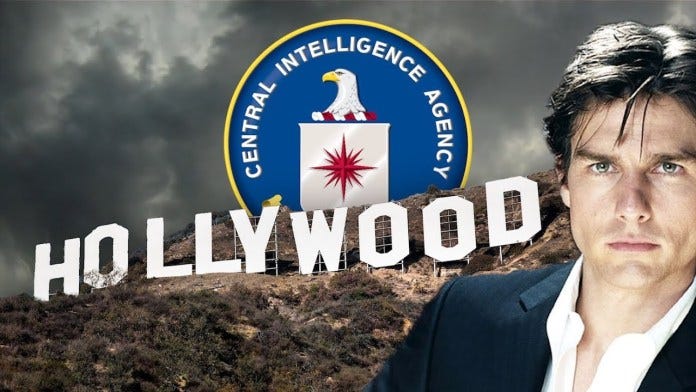 A person in a suit standing in front of a sign

Description automatically generated