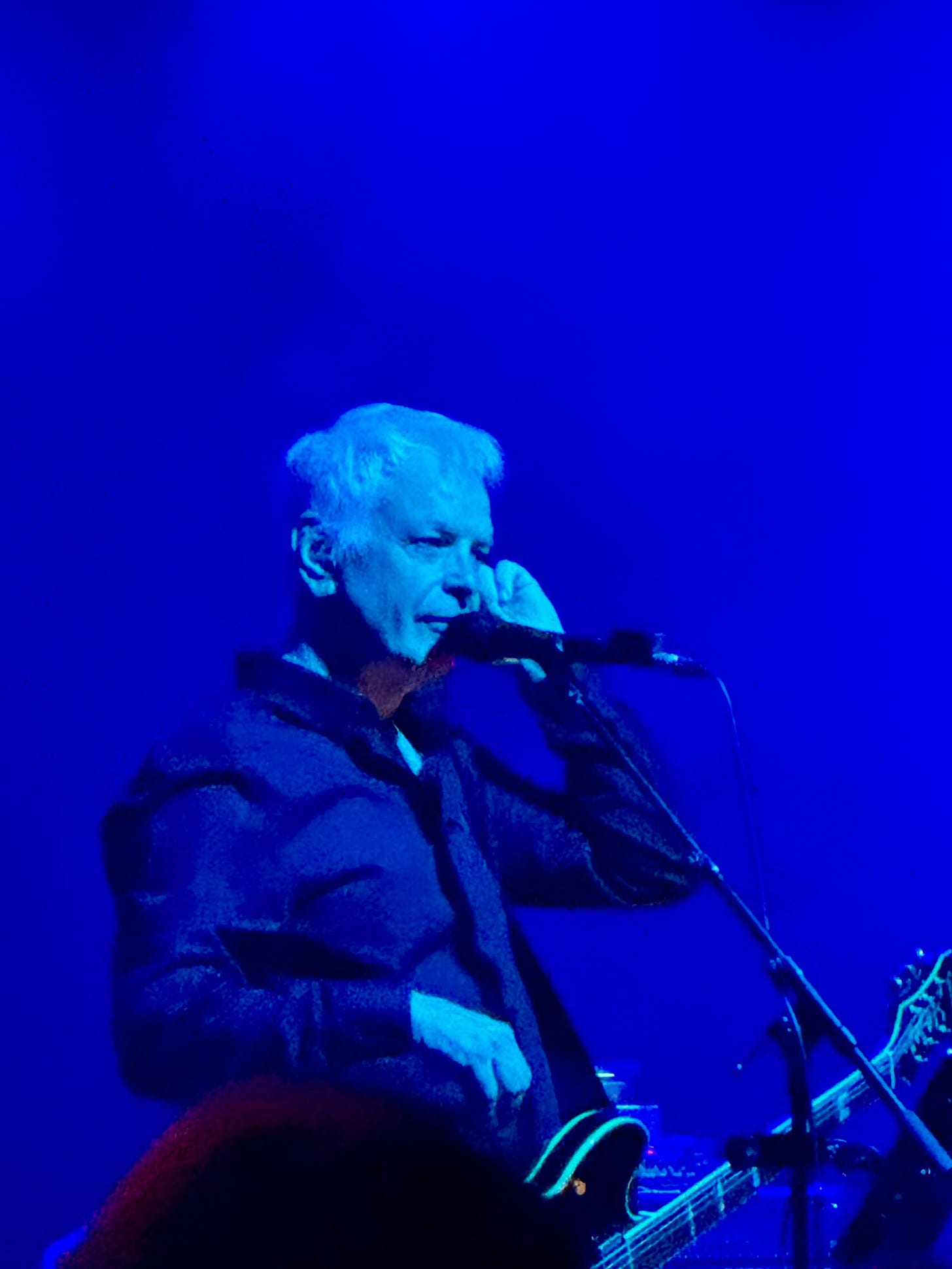 David Gedge singing and playing guitar under blue stage lights at the QMU