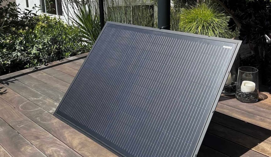 Solar panel sitting on deck with plants in the background on a sunny day