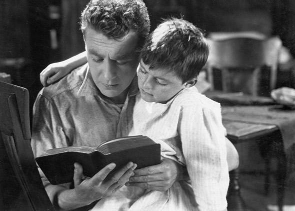 A historical photo of a father and son reading together.