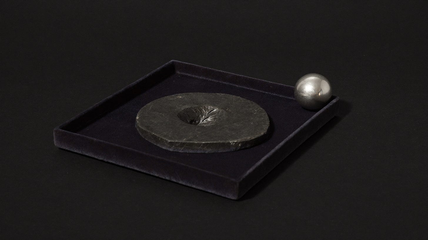 An empty round hollow in a dark tray beside a single silver sphere out of reach.