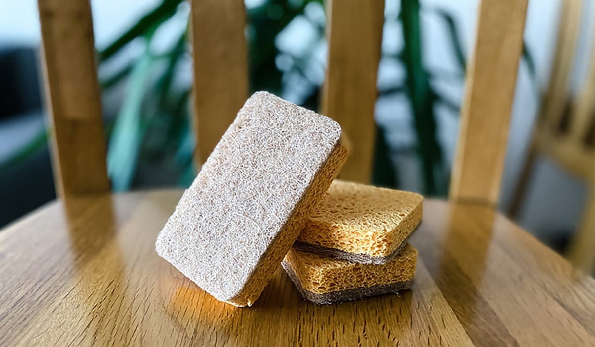 Three natural sponges are stacked on a shiny wooden surface. 
