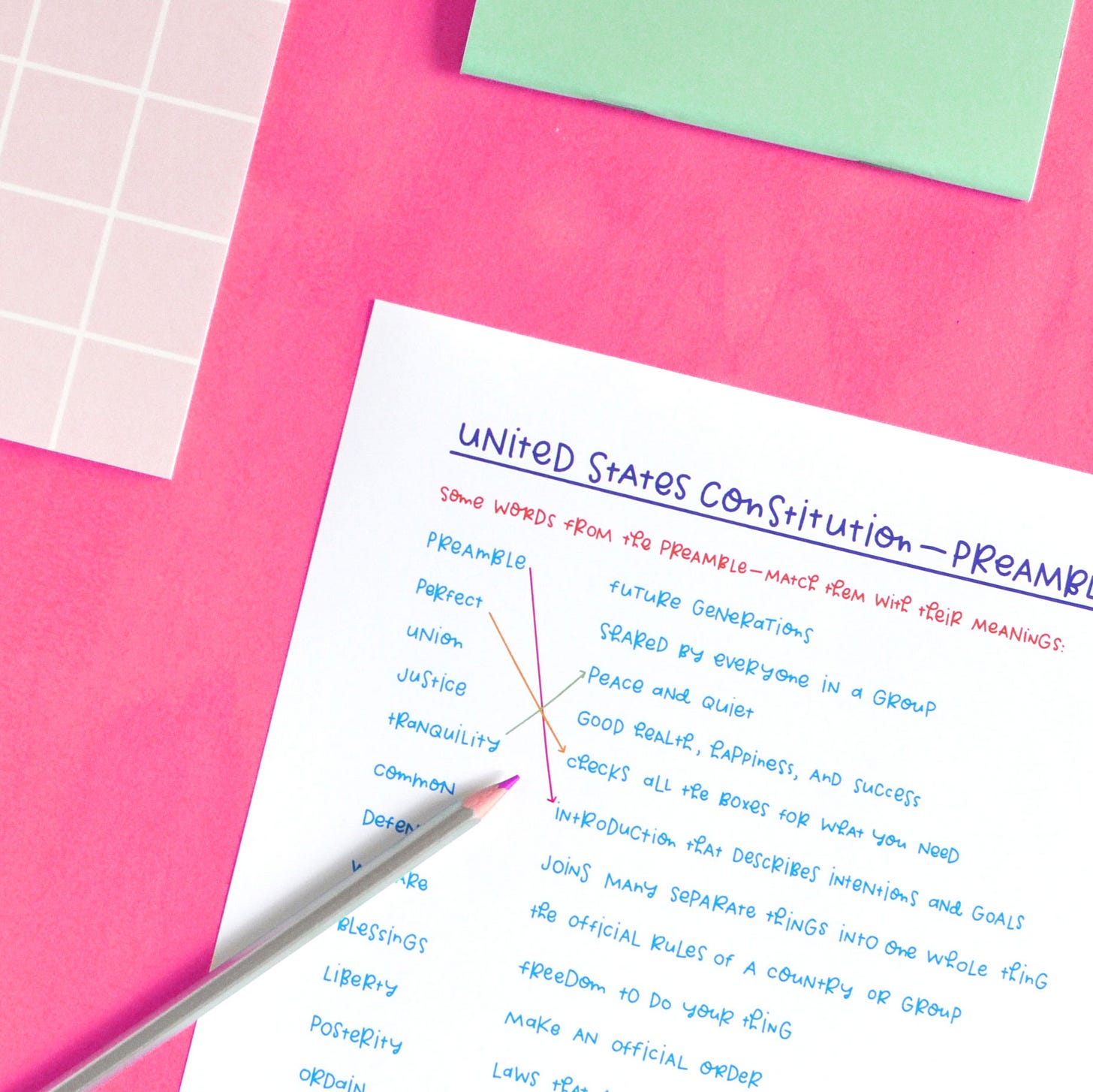 Colourful, handwritten journal page on pink background shown with colourful pencil and notebooks.