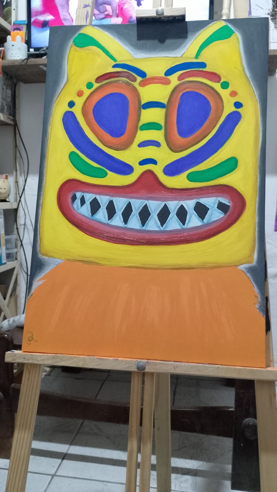 Sobre um cavalete de madeira está uma tela pintada. A pintura retrata a figura carnavalesca "La Ursa" com roupa de pelagem laranja e uma grande cabeça amarela adornada com cores que remetem às máscaras tribais africanas.