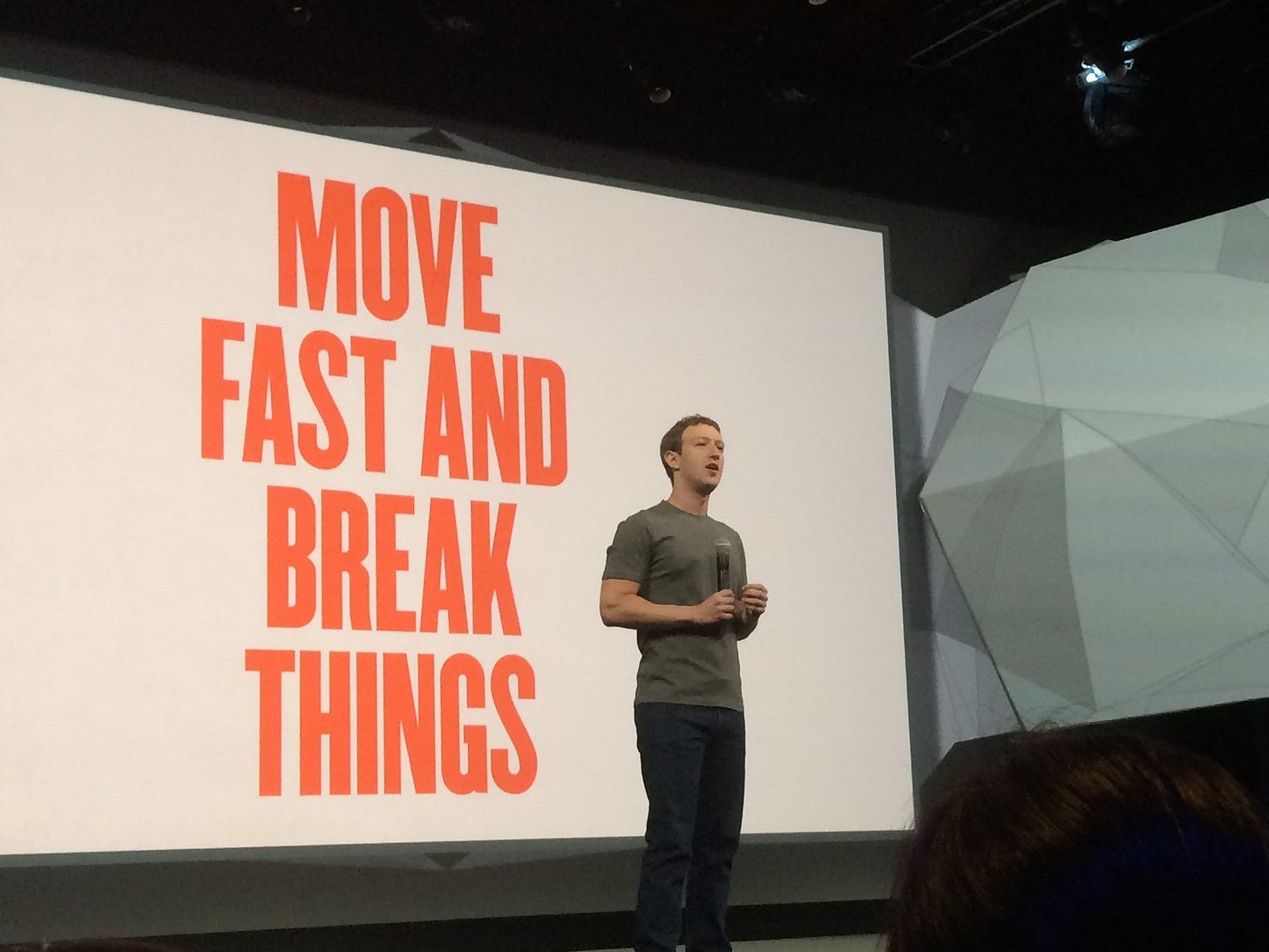 Mark Zuckerberg on stage in front of the slogan “Move fast and break things,” representing startup hustle culture.