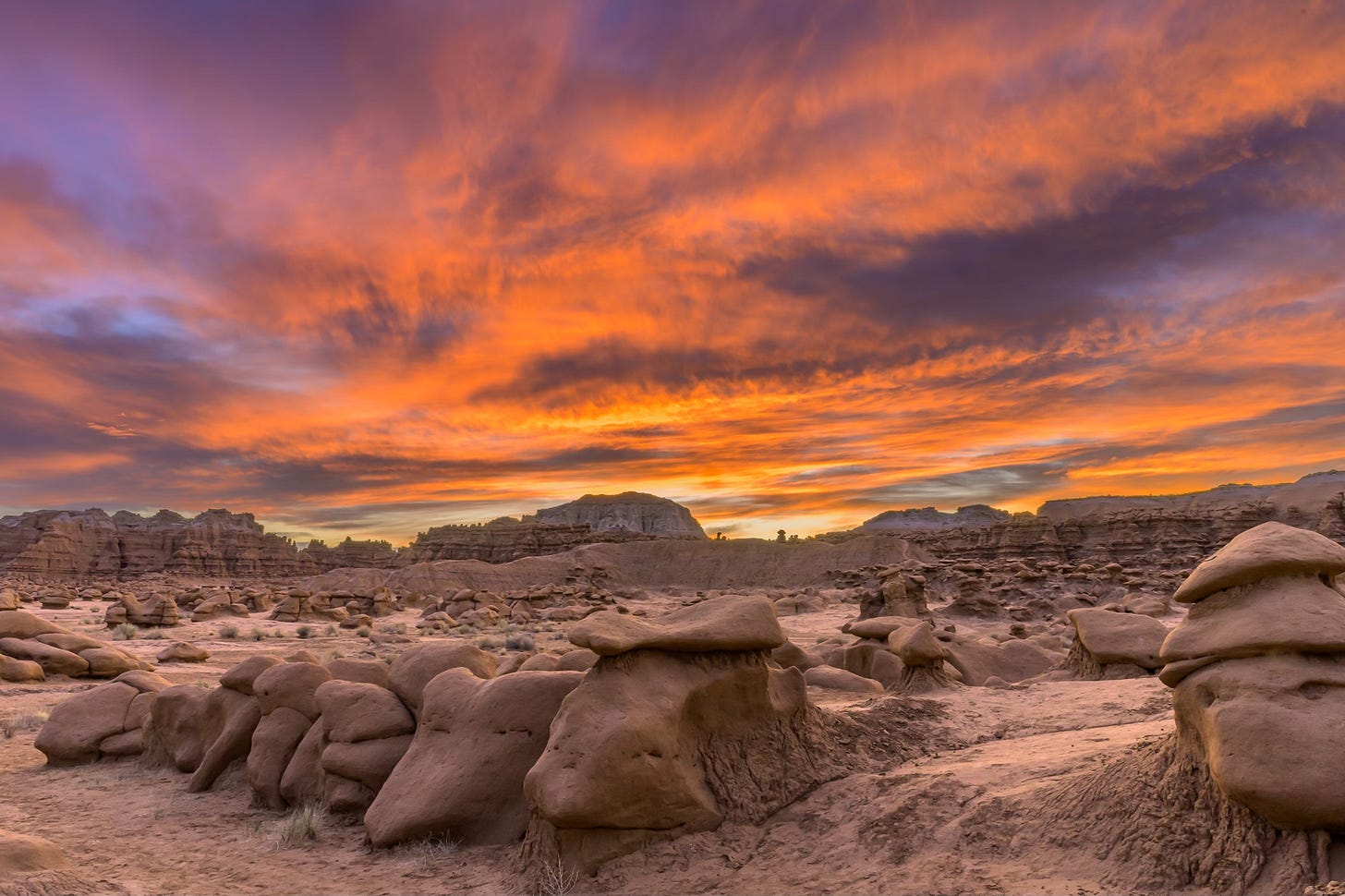 Sunrise over Goblin Valley State Park. The sky ihas clouds colored red from the sun that is about to rise. The ground has red rocks in odd shapes giving the area its name, goblin valley.