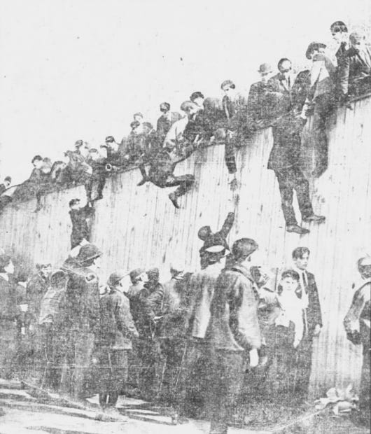 Men climbing up and sitting on the outer fence of the Huntington Avenue Grounds. Men climbing up and sitting on the outer fence of the Huntington Avenue Grounds.
