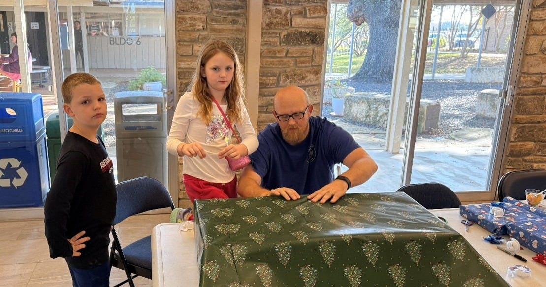 Two children, a boy and a girl help their dad wrap Christmas gifts with green paper. Two children, a boy and a girl help their dad wrap Christmas gifts with green paper.