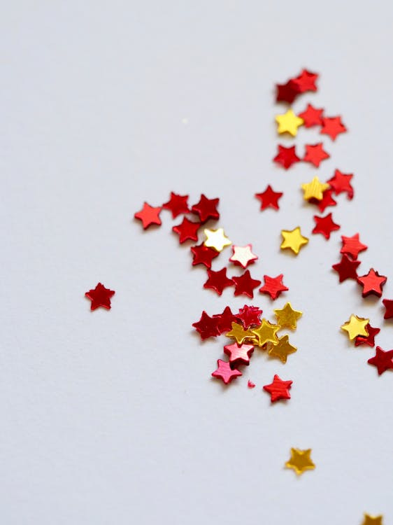Free Vibrant red and gold star-shaped confetti scattered on a plain white surface, perfect for festive and celebratory themes. Stock Photo Free Vibrant red and gold star-shaped confetti scattered on a plain white surface, perfect for festive and celebratory themes. Stock Photo