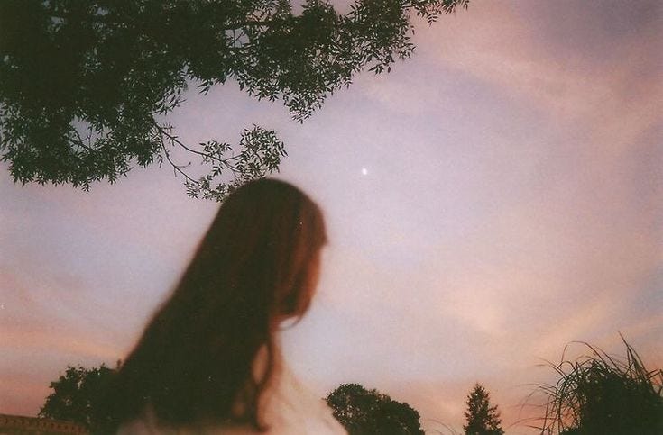 This may contain: a woman standing under a tree looking up at the sky with clouds in the background