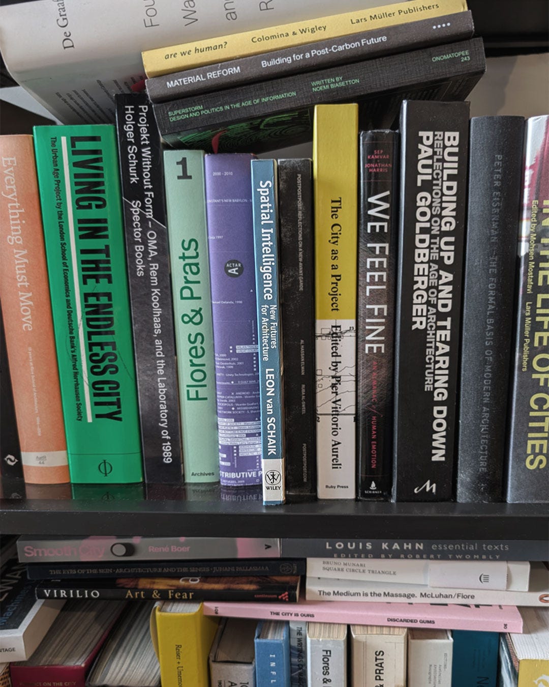 A photograph of two shelves of architectural and design books. On the upper shelf, the  teal spine of Leon van Schaik's Spatial Intelligence: New Futures for Architecture is visible among titles including Living in the Endless City, Flores & Prats, Four Walls and a Roof by Reinier de Graaf, The City as a Project, and Building Up and Tearing Down. On the lower shelf: Juhani Pallasmaa's The Eyes of the Skin, Louis Kahn Essential Texts, The Medium is the Massage, and Virilio's Art & Fear, among others.