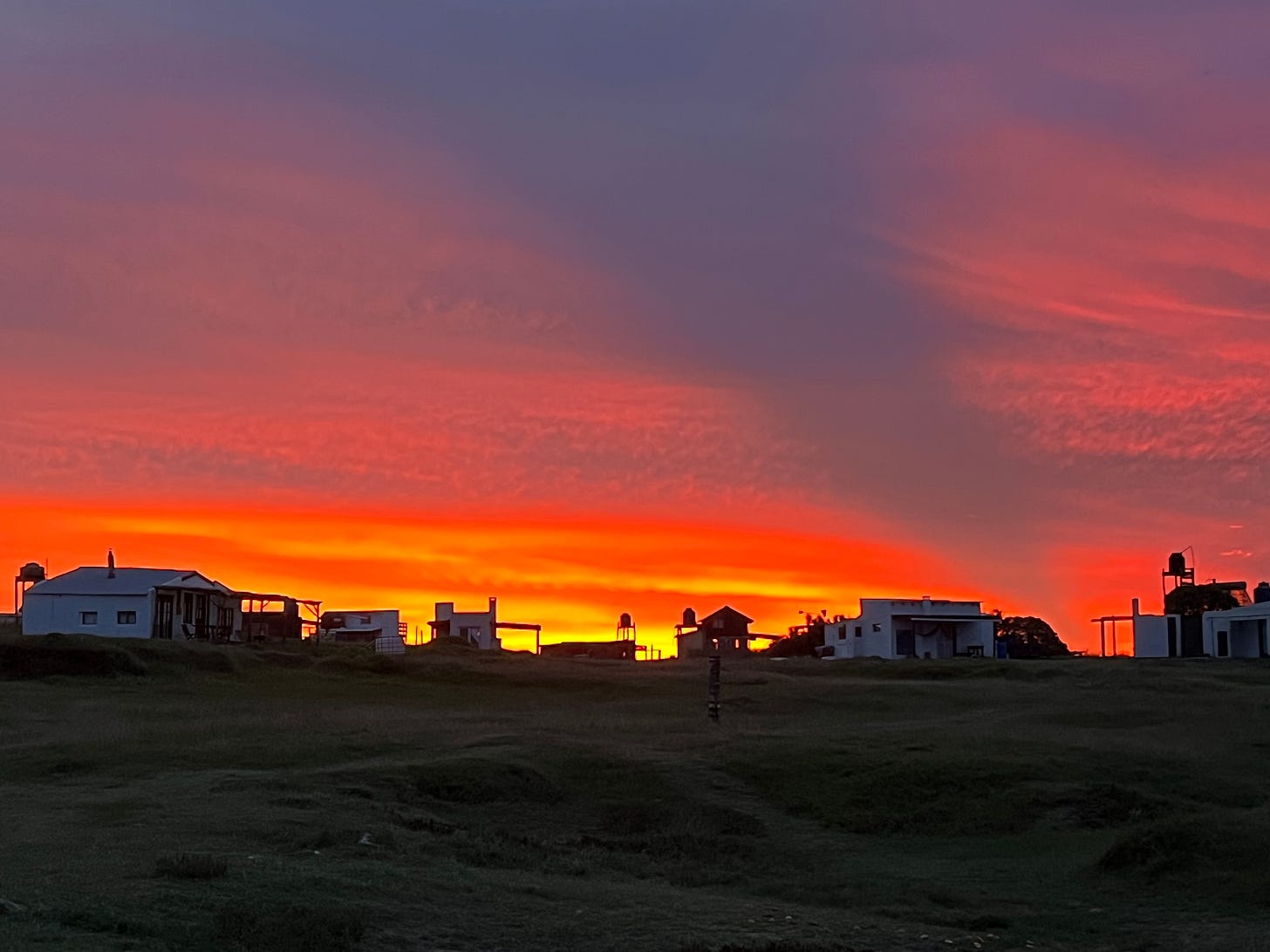 several shacks on a hill with the backdrop of a beautiful orange and red sunset in cabo polonio
