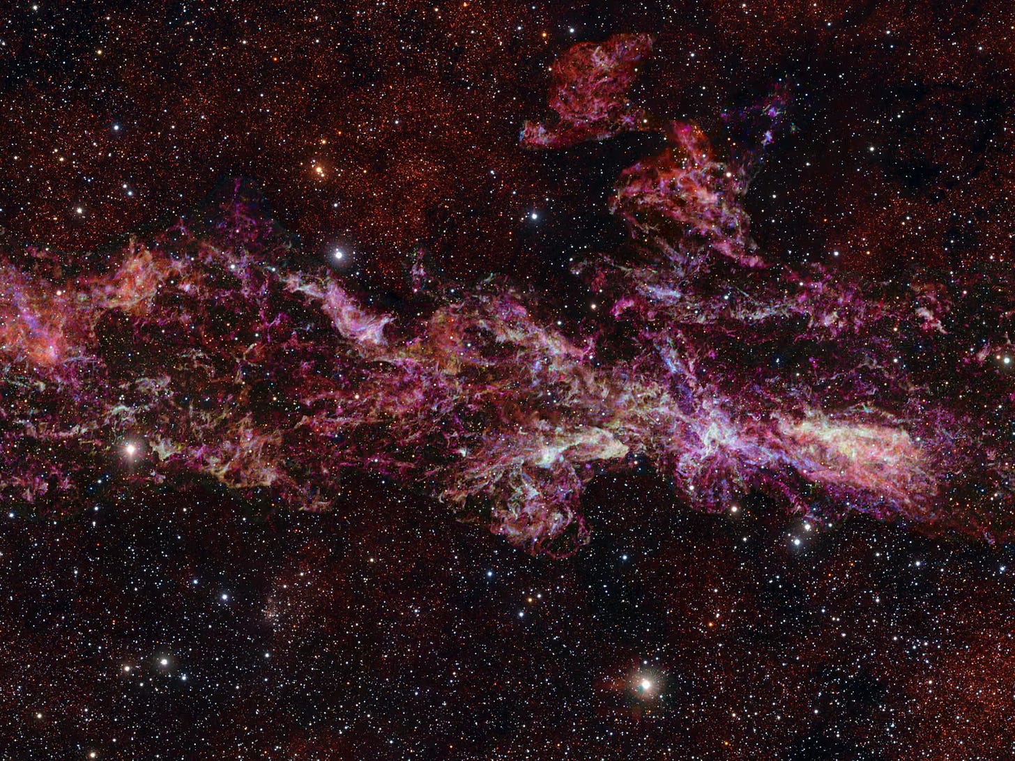 Clouds of pink and purple gas twirl around against the deep black of space, punctured with thousands of tiny white stars. 
