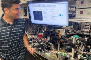 Researchers have developed a new light-based computing scheme called LightHash that reduces the energy necessary for cryptocurrency and blockchain applications. First author Sunil Pai is pictured with the optical setup used for the new research.
