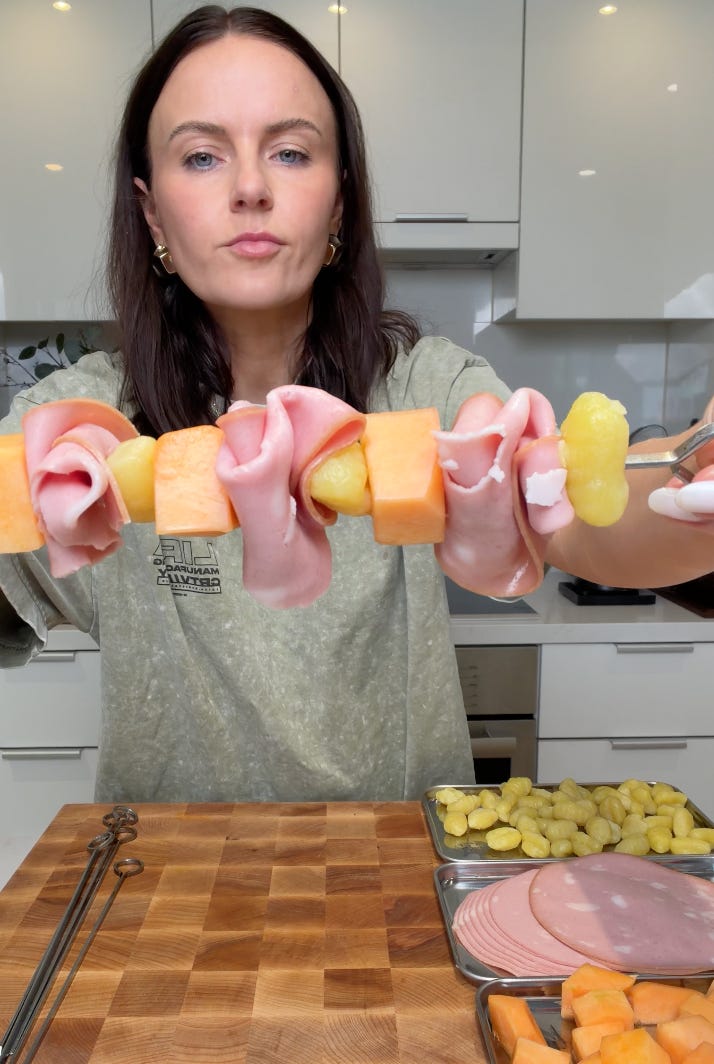 Assembled mortadella and gnocchi skewer held up to show the ruffled meat technique, Assembled mortadella, cantaloupe, and gnocchi skewers being brushed with avocado oil before grilling