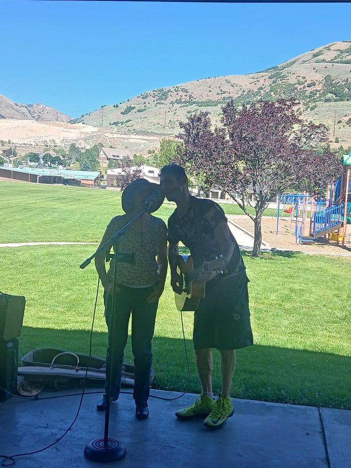 1. a man playing a guitar and singing with a woman. 2. two people standing behind a refreshments table loaded with watermelon and cookies.