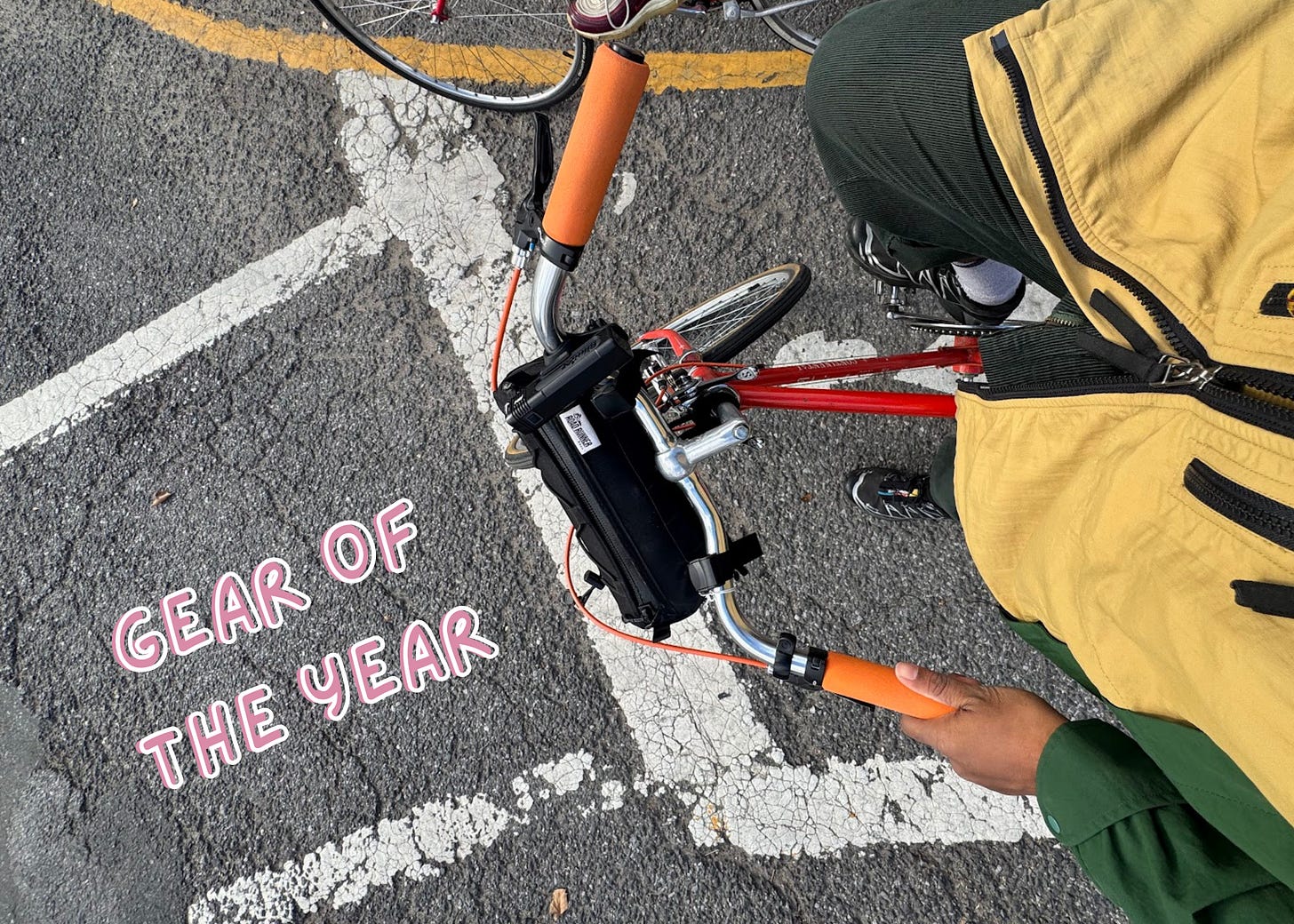 Photo of bike handlebars viewed from above with a cycling bag on them. Street is visible below. Text reads "Gear of the Year"