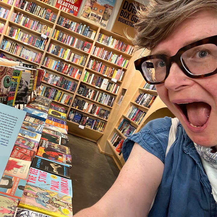 The author with their mouth agape in wonder and delight at their book in the wild in a bookstore; their book on a shelf