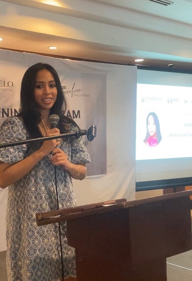 Young Filipina in butterfly sleeve dress speaking with microphone in hand at an event.