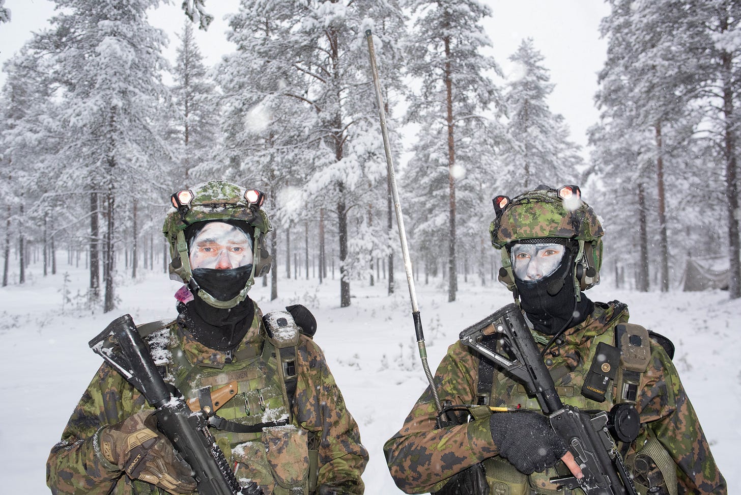 Two Finnish soldiers stand facing the camera against
a snow covered forest background. They are wearing green camouflage uniforms and helmets and holding automatic weapons pointed down against the upper half of their bodies. Their faces are covered with white camouflage paint, with the lower half covered by balaclavas. Two Finnish soldiers stand facing the camera against
a snow covered forest background. They are wearing green camouflage uniforms and helmets and holding automatic weapons pointed down against the upper half of their bodies. Their faces are covered with white camouflage paint, with the lower half covered by balaclavas.