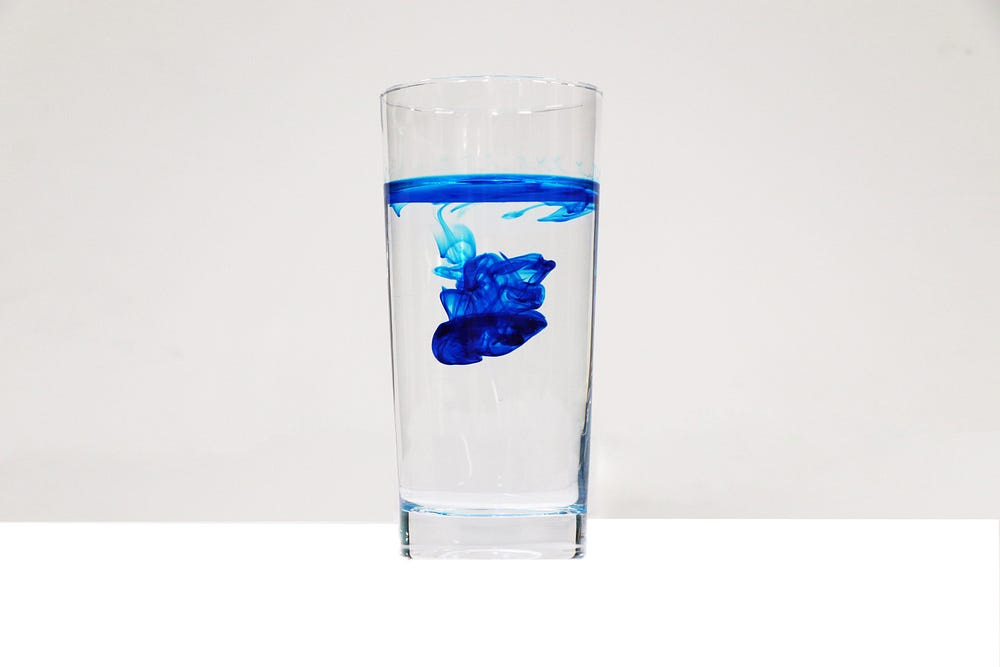 a glass of water with blue substance in it