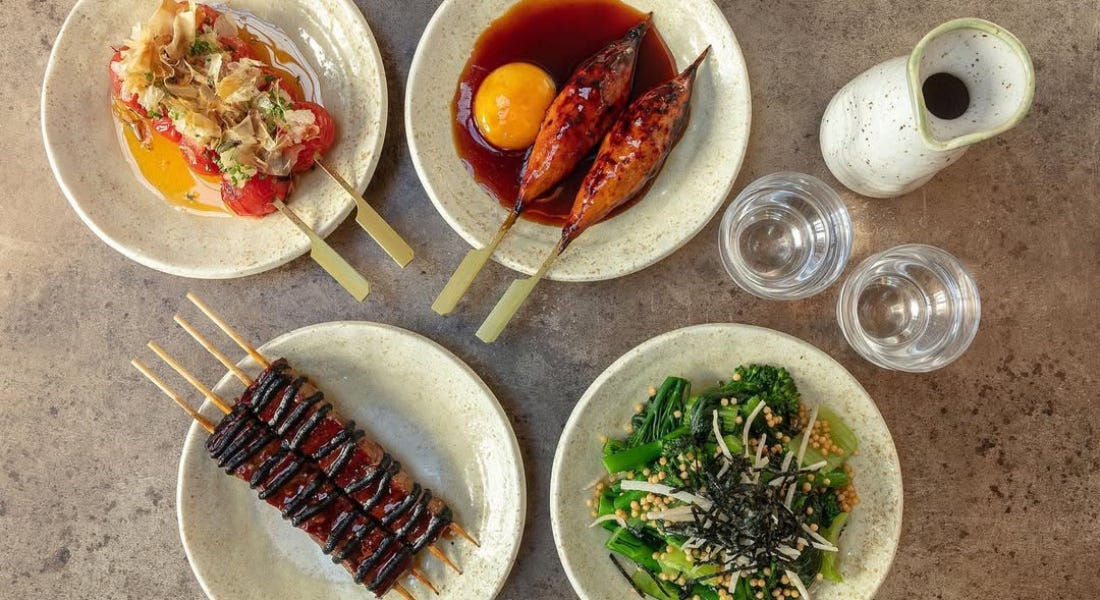 Four small plates filled with Japanese skewers and salad, on top of a grey table Four small plates filled with Japanese skewers and salad, on top of a grey table