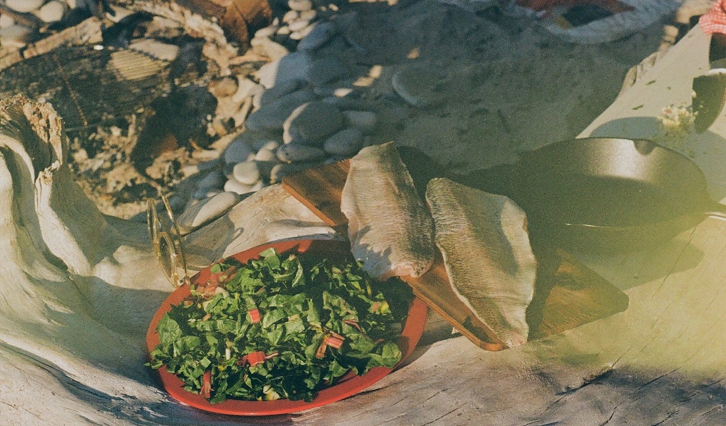 raw whitefish resting on cedar board next to plate of Swiss chard before cooking over open fire