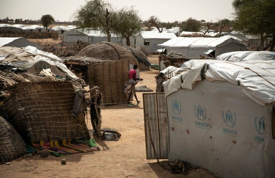 A woman walking between makeshift shelters and tents made with reeds and canvas.