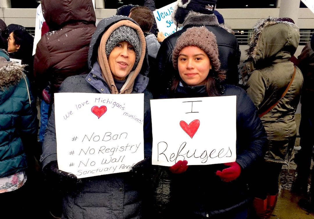 Julie and her teegaged daughter protesting the immigration ban in 2017. They are bundeled up against the winter cold and holding signs affirming immigrant and refugee rights.