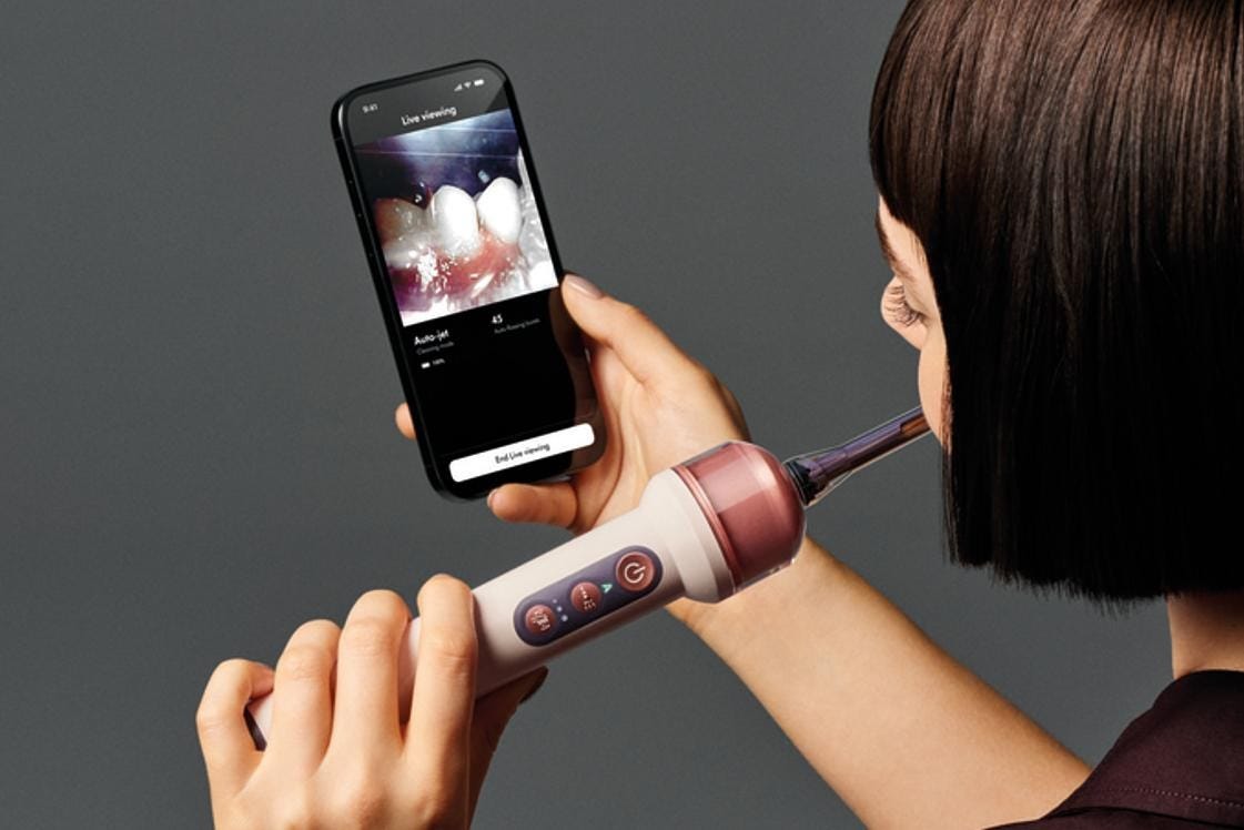 A person looks at a live video of the inside of their mouth on a smartphone while brushing with the Dyson CameraJet.