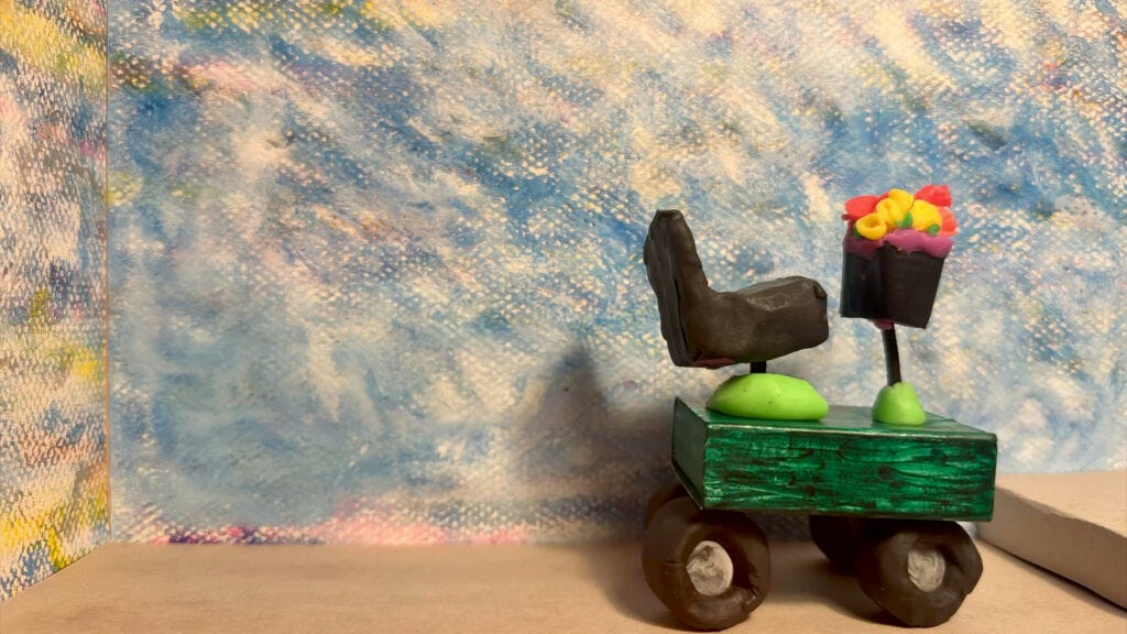 A film still showing a a diorama featuring a model of a mobility scooter meeting a raised step. A film still showing a a diorama featuring a model of a mobility scooter meeting a raised step.