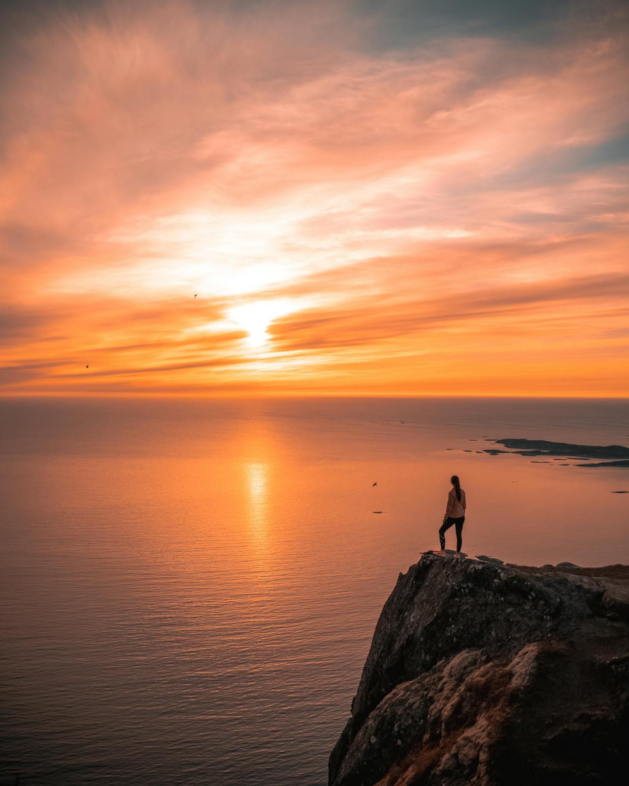 Person standing confidently on a cliff at sunset, symbolizing self-reflection and empowerment.